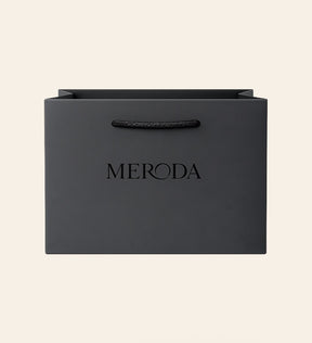 Matte zwarte Cadeautas met een geweven touwvatting en een in relief gedrukt Meroda logo op een creme achtergrond