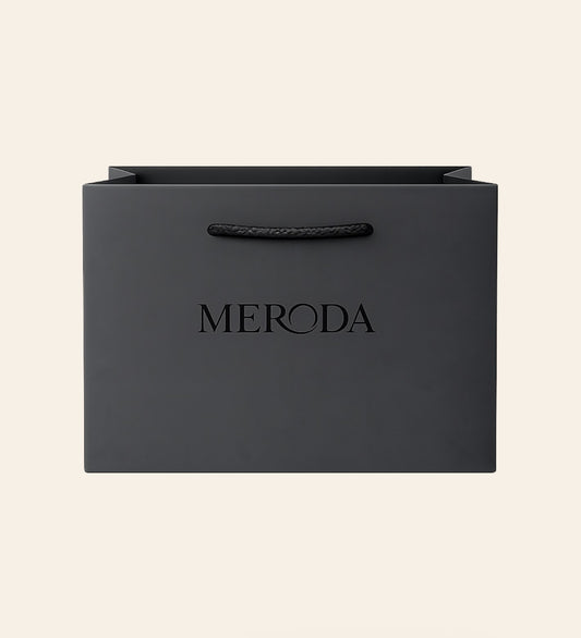 Matte zwarte Cadeautas met een geweven touwvatting en een in relief gedrukt Meroda logo op een creme achtergrond