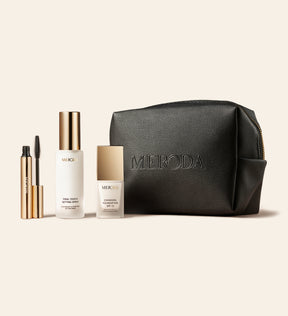 Travel Kit met Mini Gilded Lashes Mascara, Mini Final Touch Setting Spray, Mini Changing Foundation en zwarte reistas op een lichte achtergrond