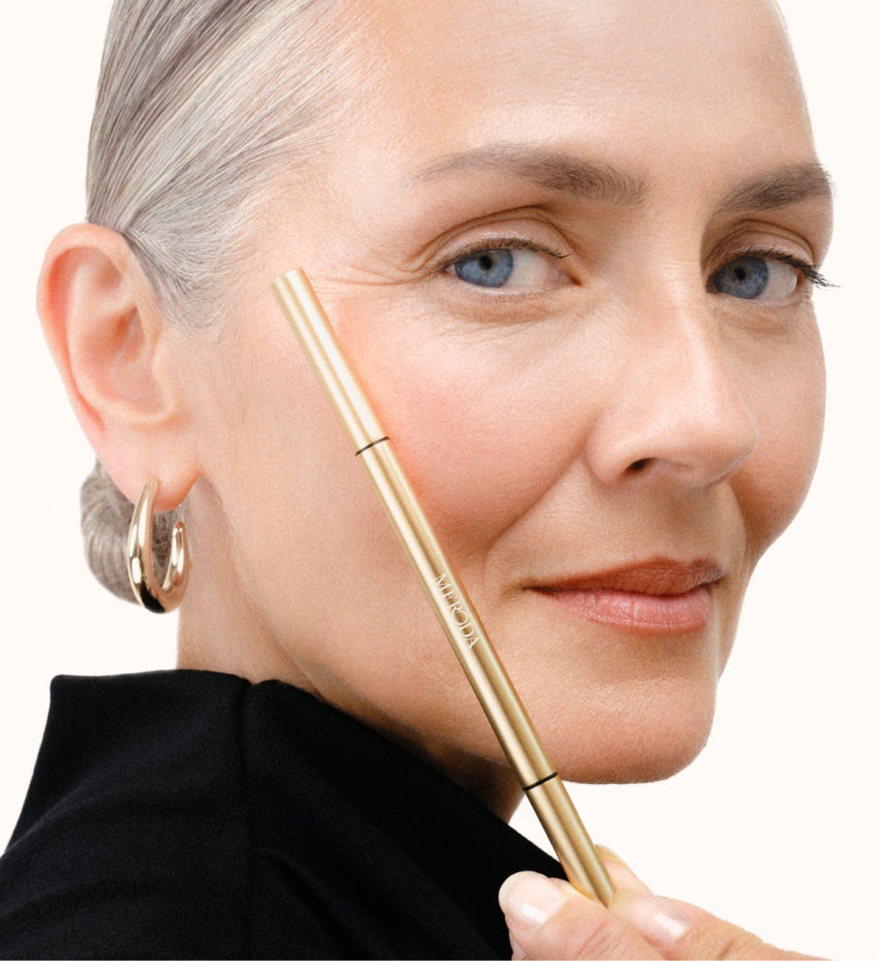 Model houdt de Precision Brow Pencil in de tint Ash naast haar gezicht