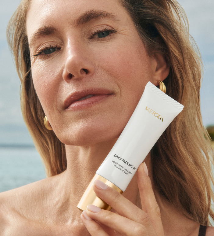 Daily Face SPF 40 tube vastgehouden door een model met een stralende huid in een zonnige strandomgeving.