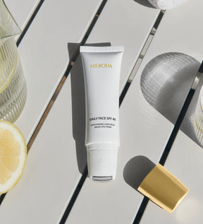 Daily Face SPF 40 tube met verkoelende metalen rollerball-applicator op een lichte tafel met een vers schijfje citroen.