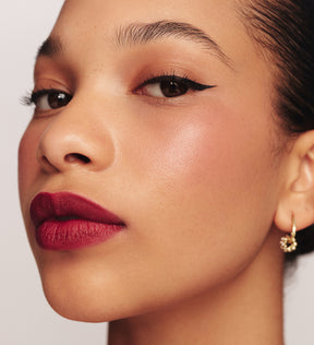 Model draagt It's All About The Wing Liquid Waterproof Eyeliner met een gedefinieerde zwarte wing en bessenkleurige lipstick